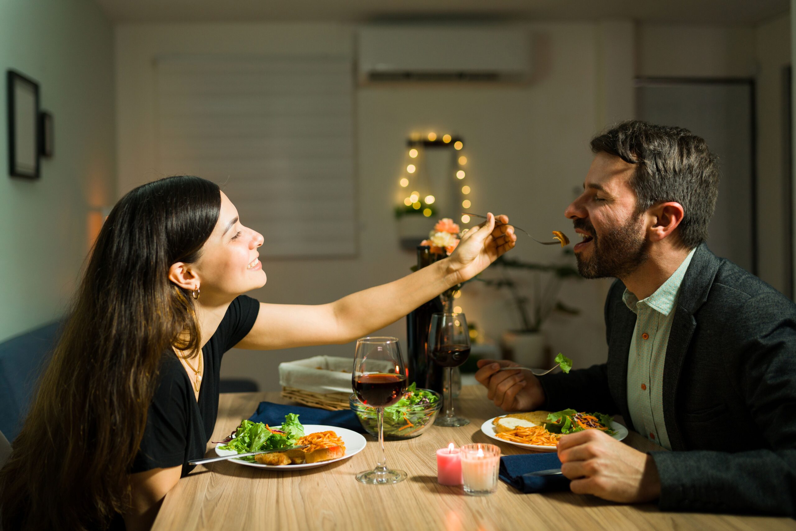 Zwei Personen sind am Essen. Die Frau gibt dem Mann etwas von ihrem Essen 